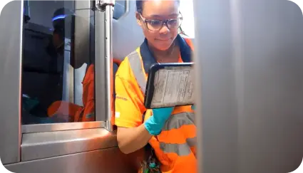 A woman wearing an orange safety vest is engaged with a tablet, showcasing operational excellence with Cubics FEnX Fare Gate