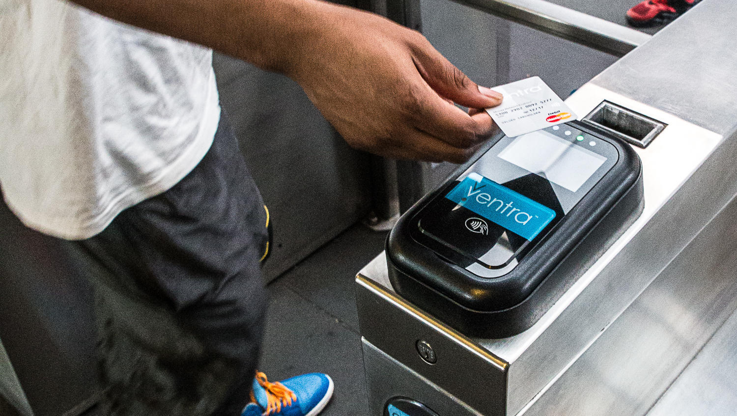 Hand tapping a debit card on Cubic's Ventra contactless fare gate